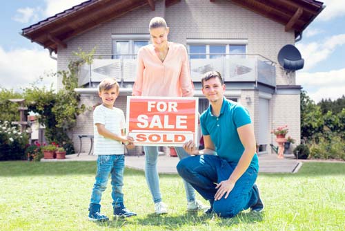 couple with daughter next to a home for sale sign in their front yard 